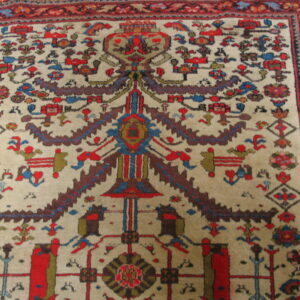 Low-pile rug with a beige field, featuring a central stylized design and geometric motifs in red, blue, and brown.