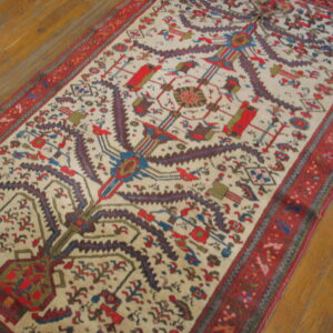 Low-pile runner rug with a cream field, stylized tree pattern, and wide red borders on wood planks.