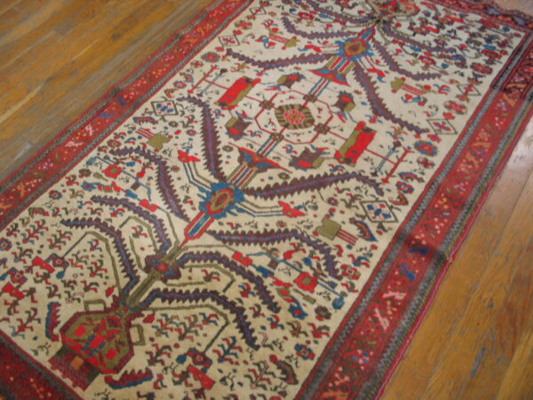 Low-pile runner rug with a cream field, stylized tree pattern, and wide red borders on wood planks.