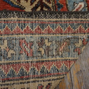 The folded corner reveals the woven backing with red, blue, and beige geometric patterns on distressed wood.