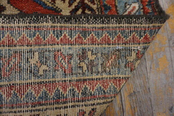 The folded corner reveals the woven backing with red, blue, and beige geometric patterns on distressed wood.