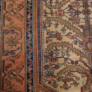 Detailed view of a low-pile rug showing a beige field and dusty rose border with complex blue and rust patterns.