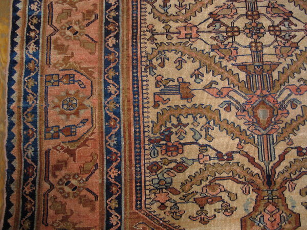 Detailed view of a low-pile rug showing a beige field and dusty rose border with complex blue and rust patterns.
