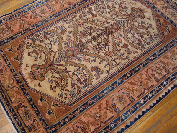 Traditional rug with tan field, rust borders, and navy accents resting on wood plank flooring.