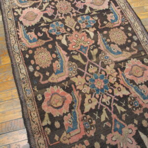 Dark runner rug with stylized floral designs in muted pink and blue on light hardwood flooring.