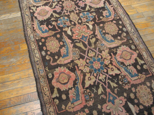 Dark runner rug with stylized floral designs in muted pink and blue on light hardwood flooring.