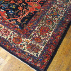 Close-up of a rug corner with complex red, navy, and cream borders lying on hardwood plank flooring.