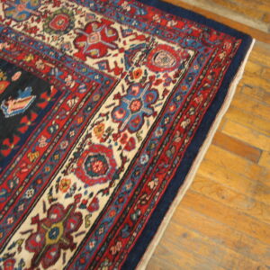 Corner detail of a patterned blue and red area rug resting on distressed light brown hardwood flooring.