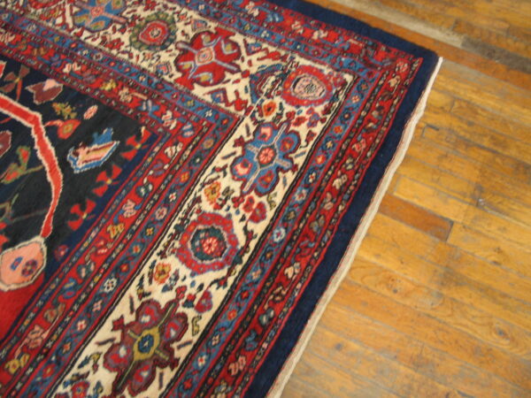 Corner detail of a patterned blue and red area rug resting on distressed light brown hardwood flooring.