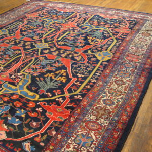 Navy rug featuring stylized red and gold figures and a detailed floral border over wood plank flooring.