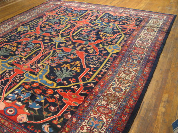 Navy rug featuring stylized red and gold figures and a detailed floral border over wood plank flooring.