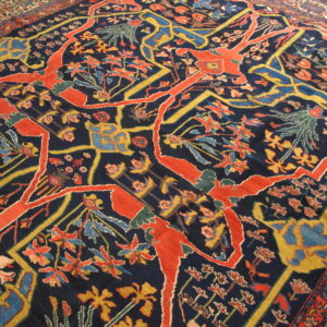 Ornate rug displaying coral red, mustard yellow, and light blue botanical motifs on a navy blue ground.