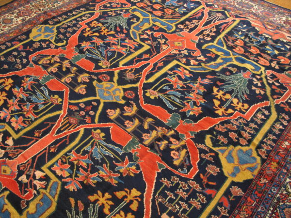 Ornate rug displaying coral red, mustard yellow, and light blue botanical motifs on a navy blue ground.