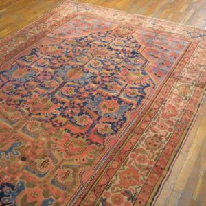 A traditional woven rug featuring deep blue, coral, and gold patterns rests on a warm wood plank floor.