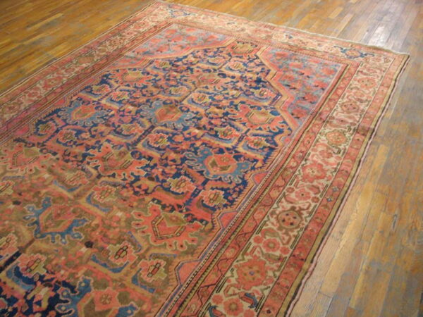 A traditional woven rug featuring deep blue, coral, and gold patterns rests on a warm wood plank floor.