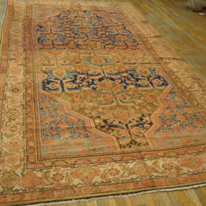 Ornate traditional rug featuring a large medallion pattern in faded pink, blue, and gold on wood flooring.