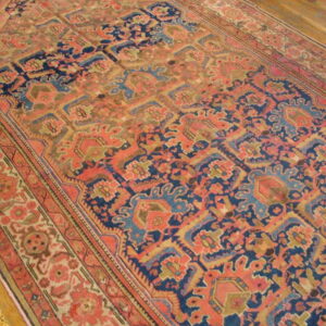 Muted coral and navy patterned rug with geometric motifs rests diagonally on light brown wood flooring.