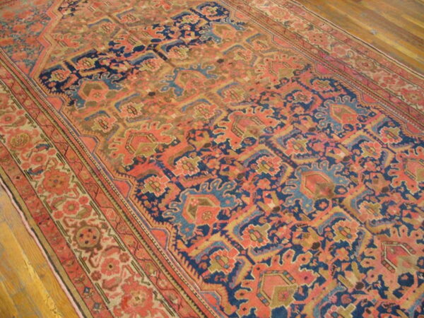 Muted coral and navy patterned rug with geometric motifs rests diagonally on light brown wood flooring.