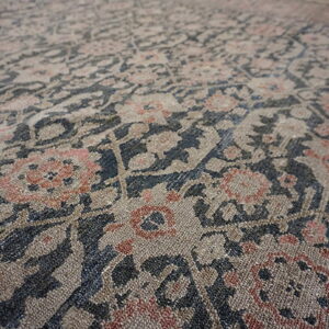 Low-pile rug detail showing a distressed floral pattern in beige, dark blue, and rust pink tones.