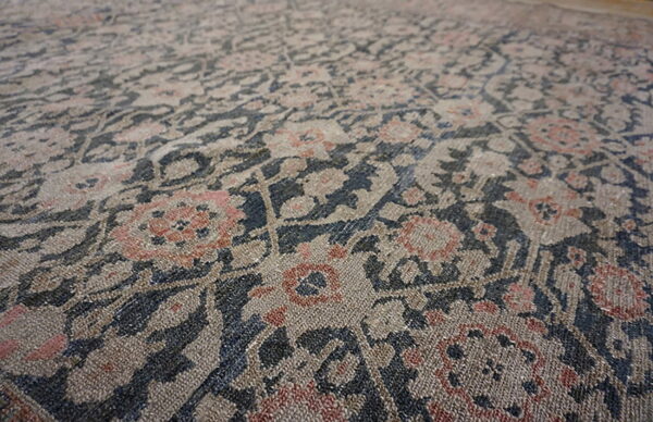 Low-pile rug detail showing a distressed floral pattern in beige, dark blue, and rust pink tones.