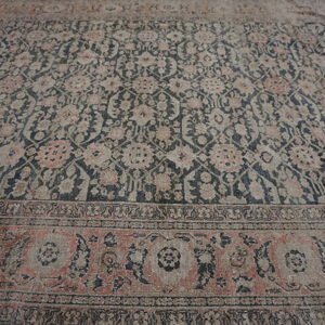 Faded area rug featuring a dense navy and gray floral pattern with terracotta accents on wood floor.