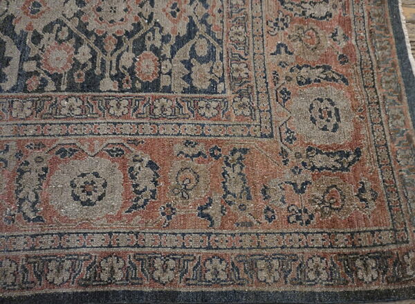 Low-pile rug corner detail with faded borders and floral patterns in navy blue, gray, and muted rust.