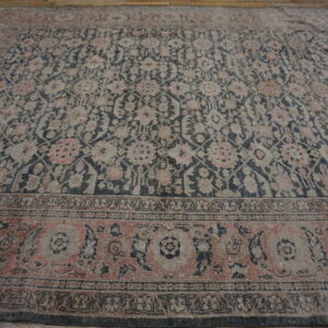 Traditional patterned rug in muted charcoal, pink, and gray tones rests on rustic wooden flooring.