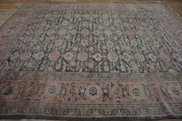 Traditional patterned rug in muted charcoal, pink, and gray tones rests on rustic wooden flooring.