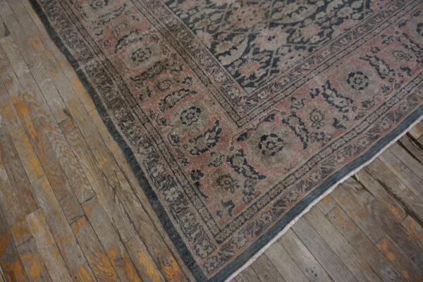 Low pile traditional rug with blue and rose floral border on weathered plank wood flooring.