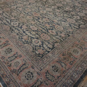 A distressed floral rug in muted navy, pink, and tan rests on rustic wide-plank wood floors.