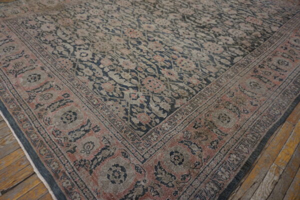 A distressed floral rug in muted navy, pink, and tan rests on rustic wide-plank wood floors.