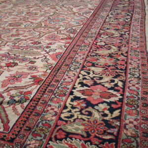 Beige and pink floral rug field meets a wide navy blue border resting on hardwood floors.