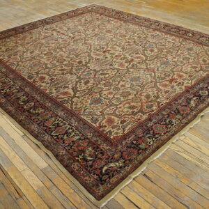 Square low-pile rug featuring a beige floral field and dark, contrasting border on worn wooden floorboards.