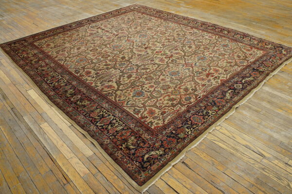 Square low-pile rug featuring a beige floral field and dark, contrasting border on worn wooden floorboards.