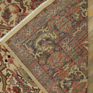 A low-pile rug with red, green, and tan motifs is folded over, showing its dark woven foundation on wood floorboards.