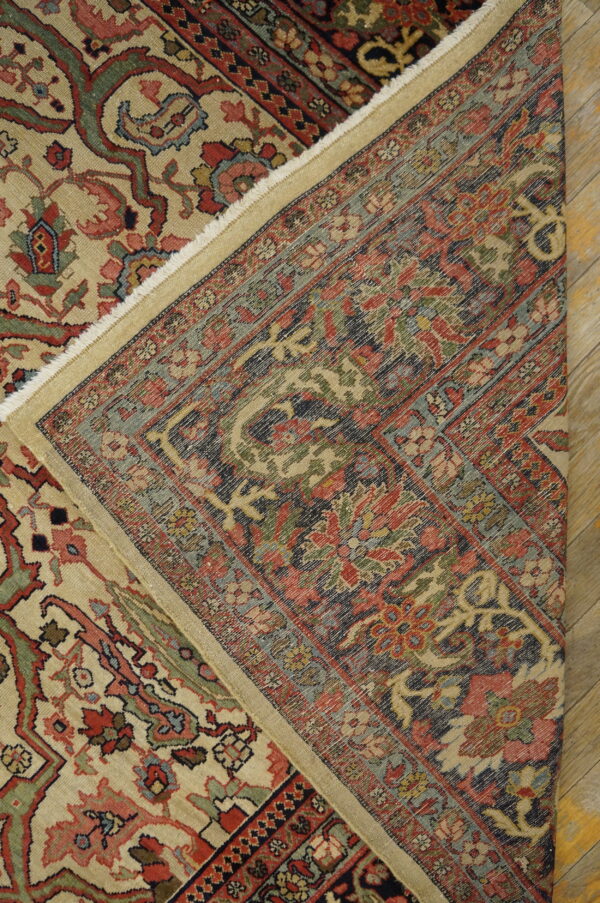 A low-pile rug with red, green, and tan motifs is folded over, showing its dark woven foundation on wood floorboards.