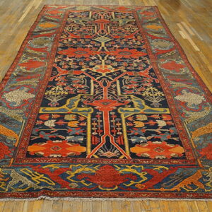 Long, low-pile rug with a complex navy, red, and yellow traditional design centered on a wood plank floor.