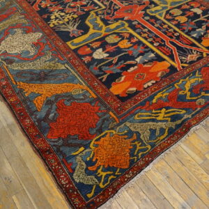 A corner of a dark blue, red, and gold patterned rug lies on weathered plank wood flooring.