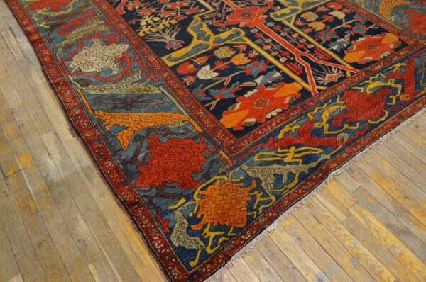 A corner of a dark blue, red, and gold patterned rug lies on weathered plank wood flooring.
