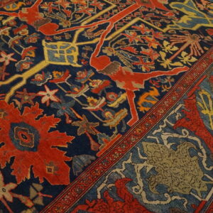 Detailed view of a navy rug with red, gold, and blue intricate patterns, featuring figures and medallions on wood flooring.