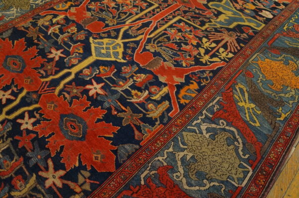 Detailed view of a navy rug with red, gold, and blue intricate patterns, featuring figures and medallions on wood flooring.
