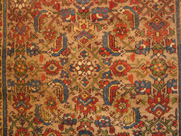 Traditional high-pile rug detail with a tan field and red, blue, yellow, and green floral geometric motifs.