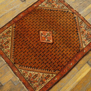 Orange and black floral patterned rug with light borders displayed diagonally on distressed wood flooring.