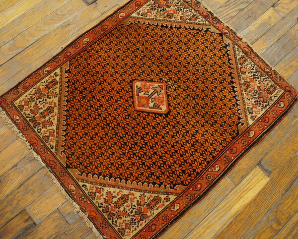 Orange and black floral patterned rug with light borders displayed diagonally on distressed wood flooring.