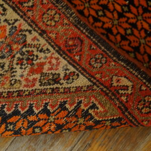 A geometric rug in red, orange, black, and tan is partially rolled back on distressed wood flooring.