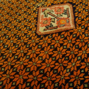 Close-up showing a dense orange and black repeating pattern surrounding a colorful, stylized square panel.