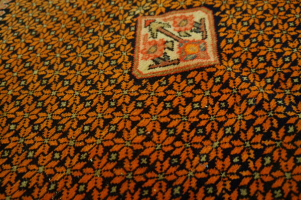 Close-up showing a dense orange and black repeating pattern surrounding a colorful, stylized square panel.