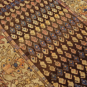 Traditional dark brown rug featuring blue and cream abstract patterns and wide floral tan borders on wood floor.