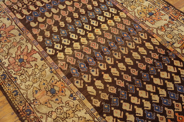 Traditional dark brown rug featuring blue and cream abstract patterns and wide floral tan borders on wood floor.