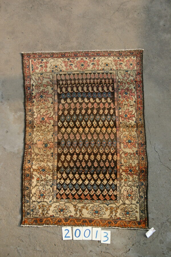 A small rug with a dark geometric center and a cream border featuring pink and blue floral designs on gray concrete.